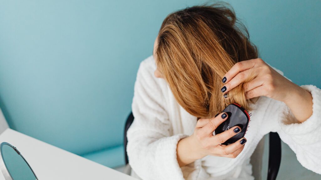 A middle aged woman brushes her hair with a comb.